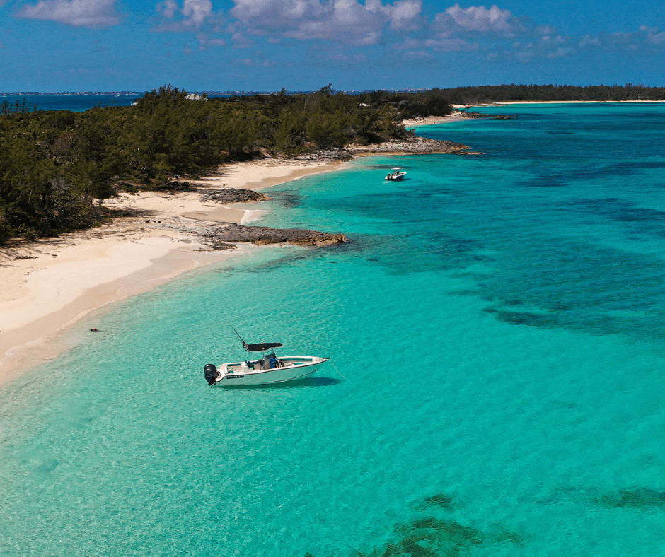Motorboot inmitten türkisblauem Wasser neben einem Sandstrand mit grüner Landschaft auf den Bahamas 