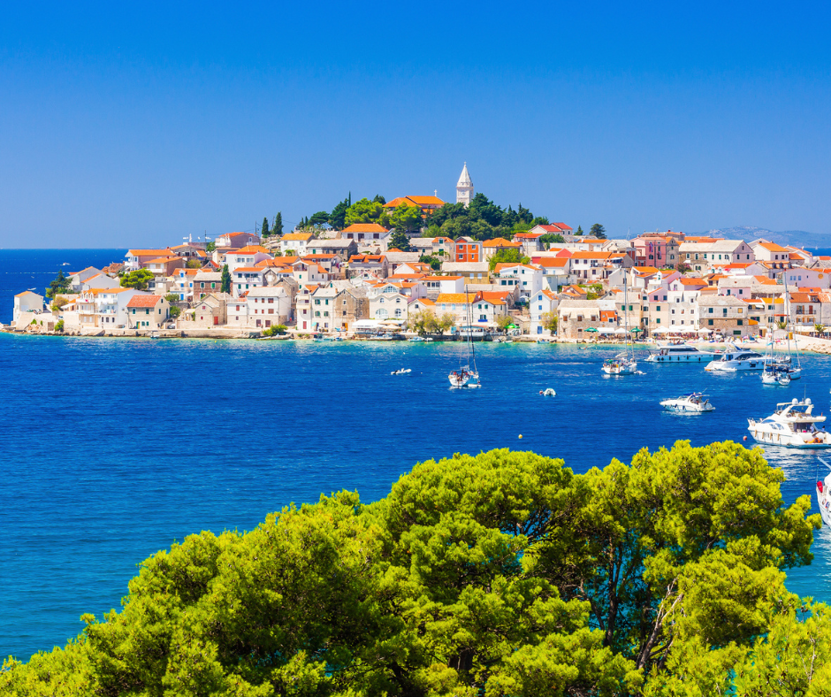 Segeltörn Mitteldalmatien, Insel Primosten - Blick auf die Stadt mit farbenfrohen Häusern, Motorboote und Segelboote auf dem azurblauen Wasser