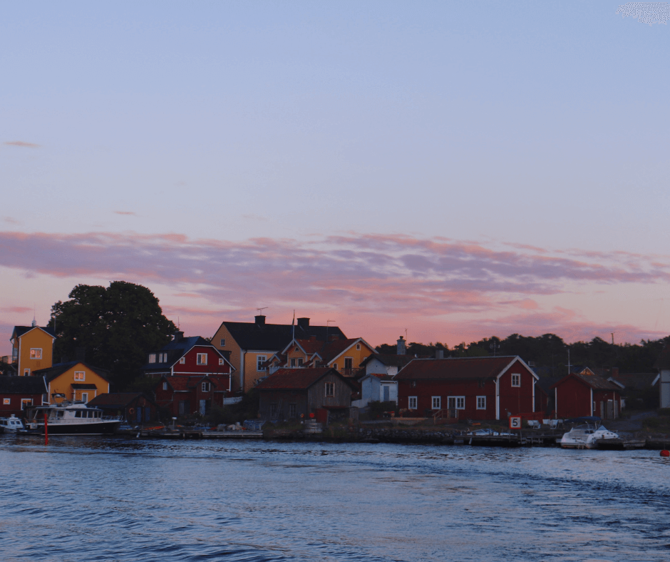 Häuser mit Booten am Steg in Sandhamn bei pinkem Himmel und abentlicher Dämmerung