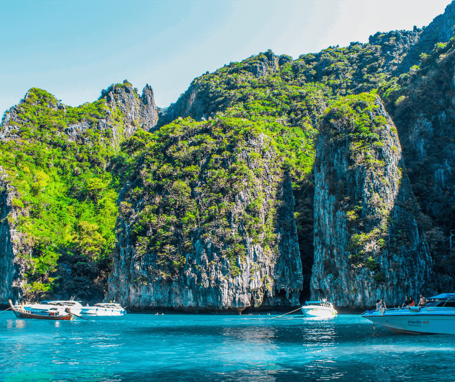 Ko Phi Phi Le, Thailand - Bewachsene Klippen ragen aus dem türkisblauen Wasser, Motorboote mit Passagieren auf dem Wasser 