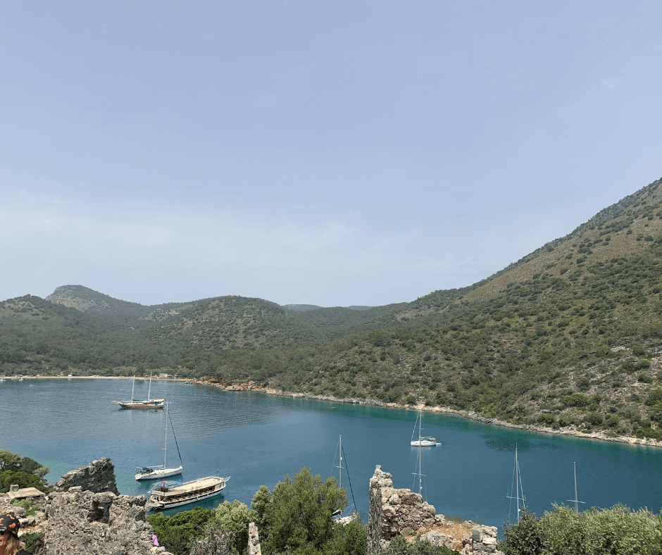 Verschiedene Boote in einer von grün bewachsenen Felsen umgebenen Bucht in der Türkei vor Anker