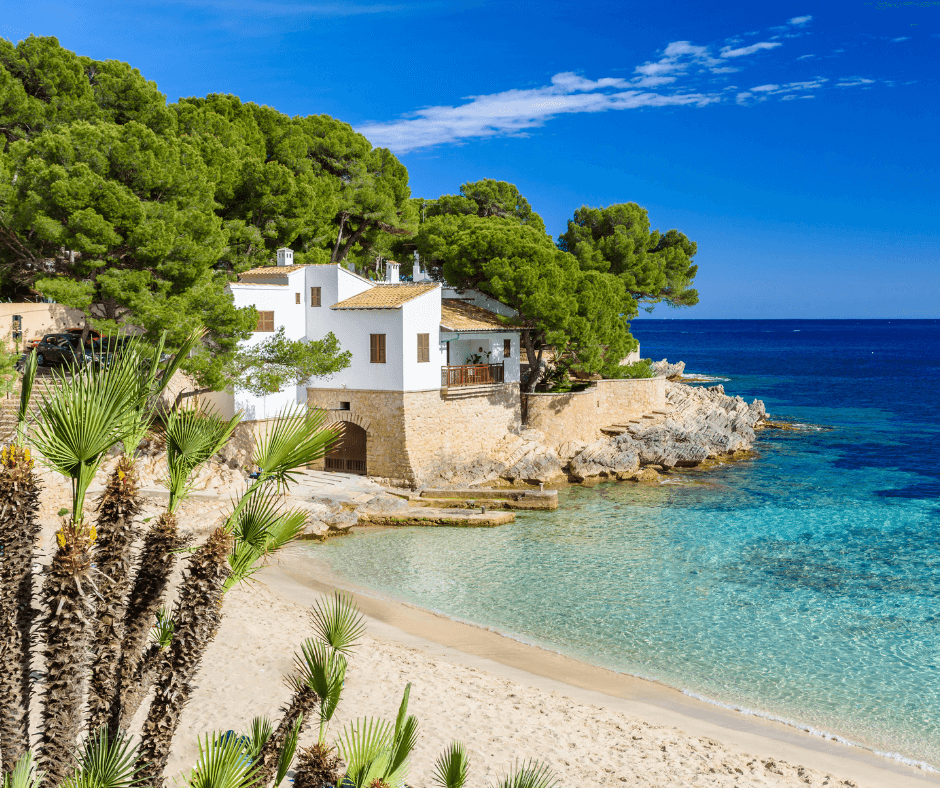 Segeltörn Mallorca - Cala Ratjada, weißes Haus am Strand mit Bäumen im Hintergrund, türkisblaues Wasser, 