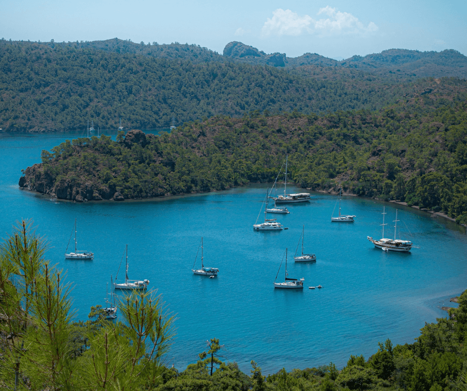 weiße Segelboote vor Anker in einer Bucht von Datca in der Türkei mit blauen Wasser und grünen Bäumen 