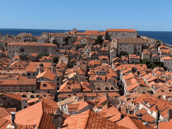 Die Altstadt von Dubrovnik aus der Vogelperspektive mit vielen alten Steinhäusern mit organgenen Dächern und dem blauen Meer und Himmel im Hintergrund