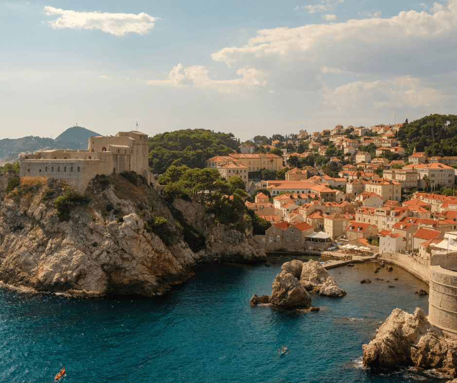 Die felsige Küste von Dubrovnik, welche mit orangen Steinhäusern bebaut ist, die bis in die Berge hineinreichen. 