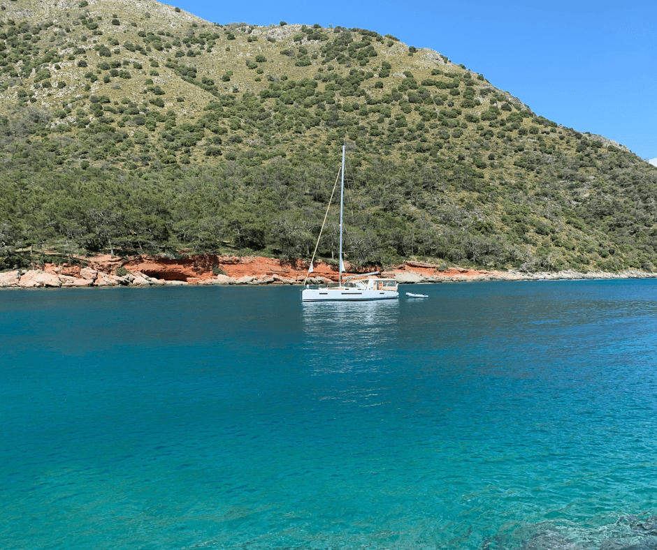 Ein weißes Segelboot an der grün bewachsenen, felsigen Küste der Türkei vor Anker im blauen Meer 