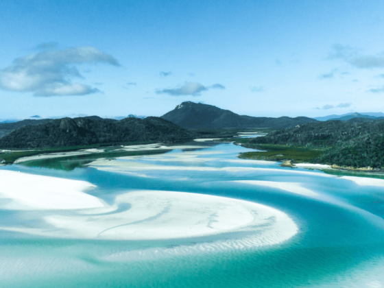 Whitsunday Islands mit weißem Sand und türkis-farbendem Wasser und grün bewachsenen Bergen im Hintergrund