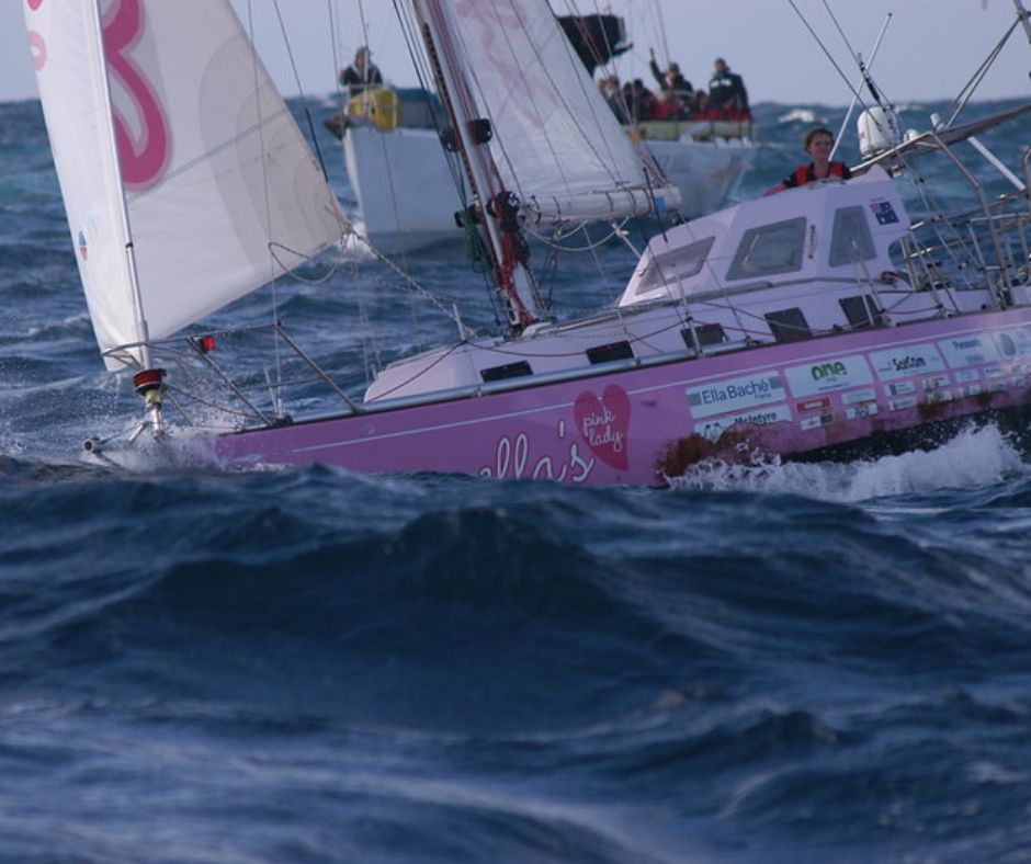 Auch dieses Boot gehört nun zu den berühmten Segelyachten. Meer mit Wellen. Darauf sieht man zwei Boote. Im Vordergrund pinke Boot "Pink Lady" mit einem 19-jährigen Mädchen darauf. Auf dem Boot im Hintergrund sitzen mehrere Menschen. 
