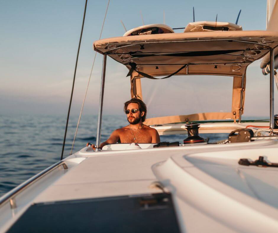 Mann mit Sonnenbrille in einem Boot. Im Hintergrund ist das Meer bei Sonnenuntergang.
