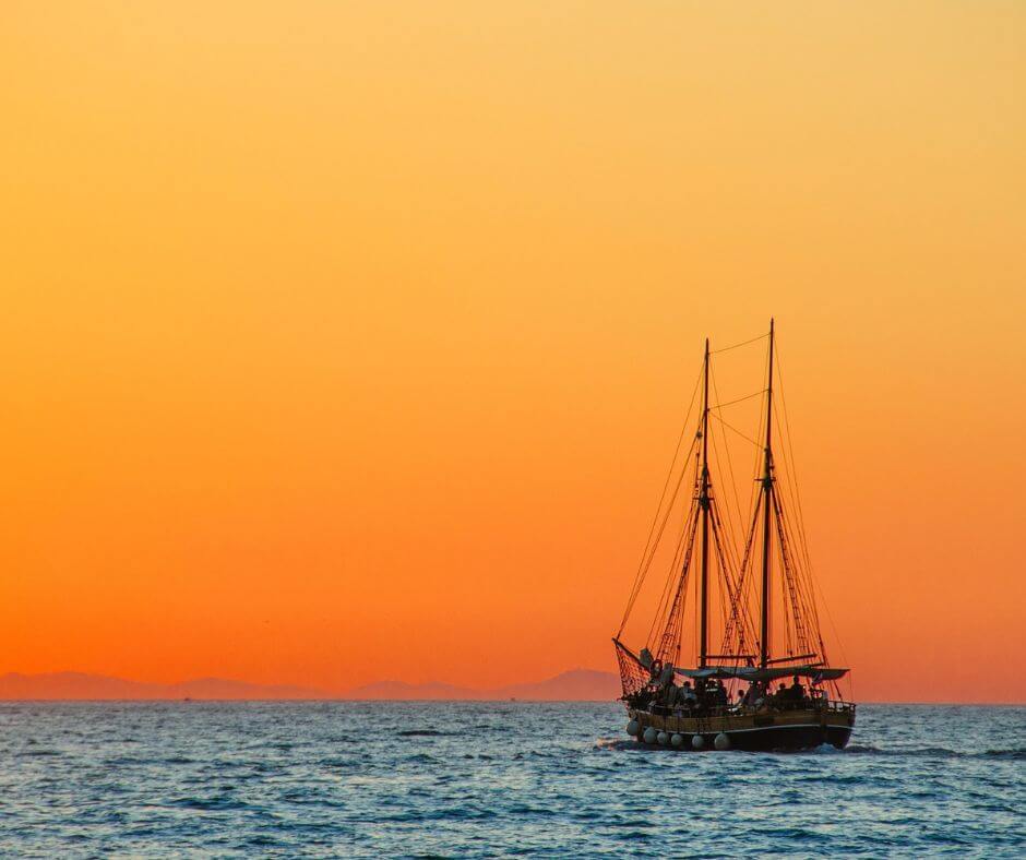 Ein altertümliches Schiff auf dem Meer, welches in den Sonnenuntergang fährt