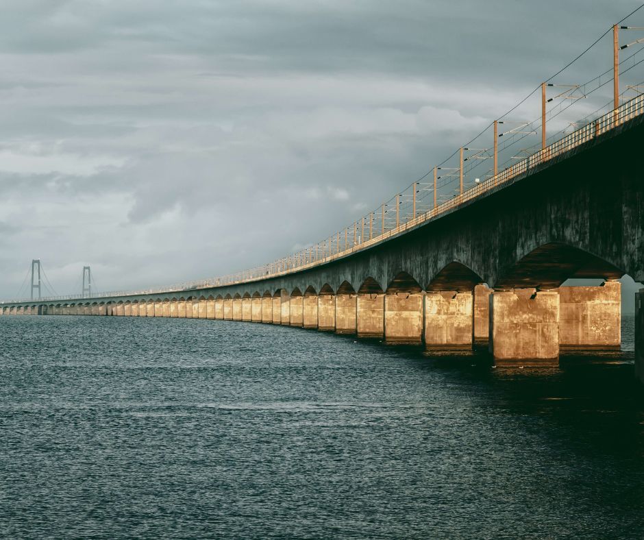 Die auf dem Meer gebaute, betonierte Belt-Brücke zieht sich quer durch das Bild. Im Hintergrund sind dunkle Wolken am Himmel.