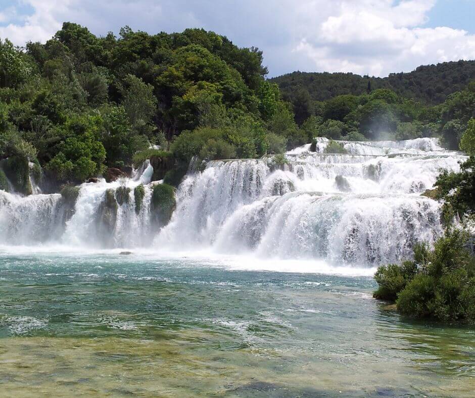 Wasserfälle umgeben von grünen Bäumen, der in einem Becken münden.