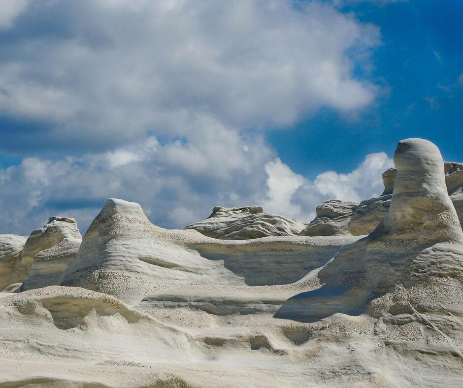 Weiße Felsen auf Milos in ungewöhnlichen Formen. Im Hintergrund sieht man blauem Himmel mit weißen Wolken.