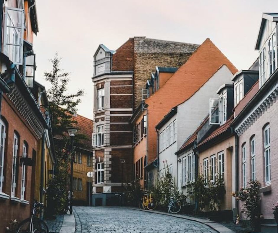 Kleine Straße mit Kopfsteinpflaster in Odense. Nordische Hausfassaden aus Backstein, teilweise mit weißen Rosenstöcken bewachsen. 