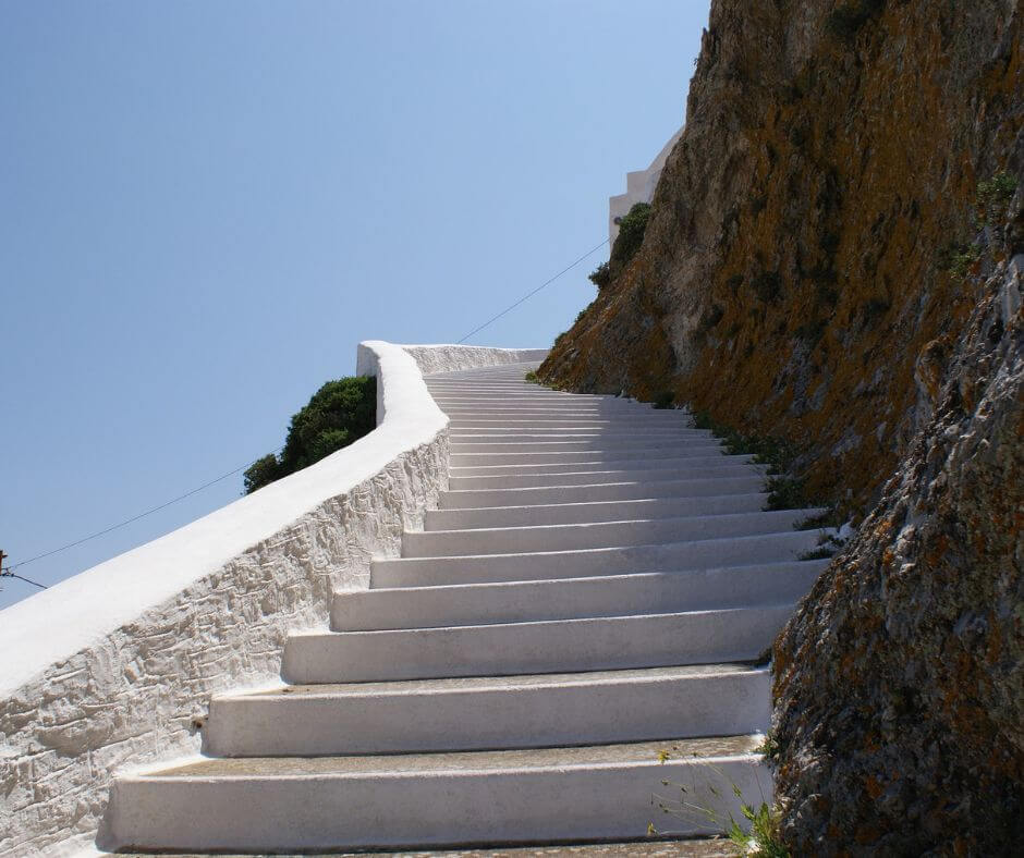 Eine weiße Treppe, die scheinbar in den Himmel führt.Rechts sieht man eine felsige Steinwand.