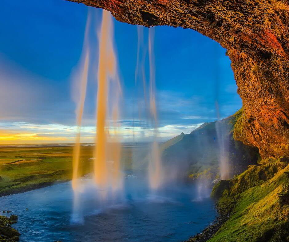 Wasserfall in Island, einem weiteren guten Ort für Whale Watching in Europa. Man sieht einen Sonnenuntergang. Das Bild wird seitlich von Gestein eingerahmt.