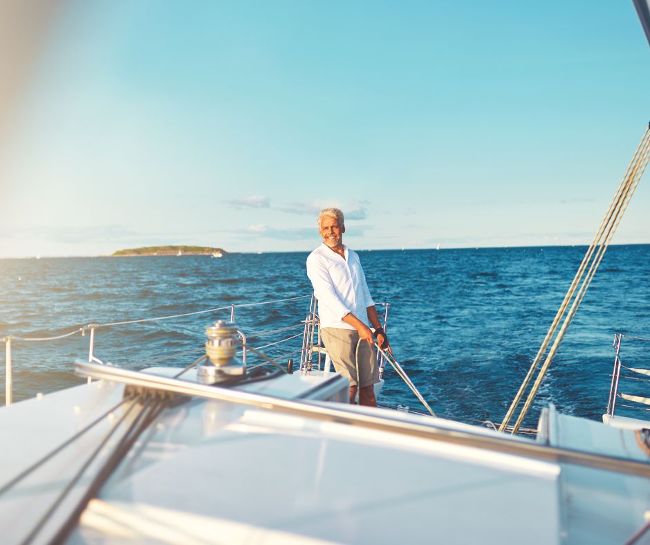 Ein männlicher Skipper auf einem Boot. Im Hntergrund sieht man das Meer und eine kleine Insel