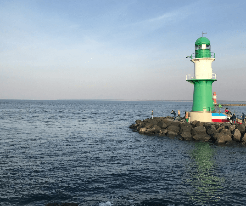 Leuchturm in Warnemünde in grün direkt am Meer mit Personen die Bilder machen 